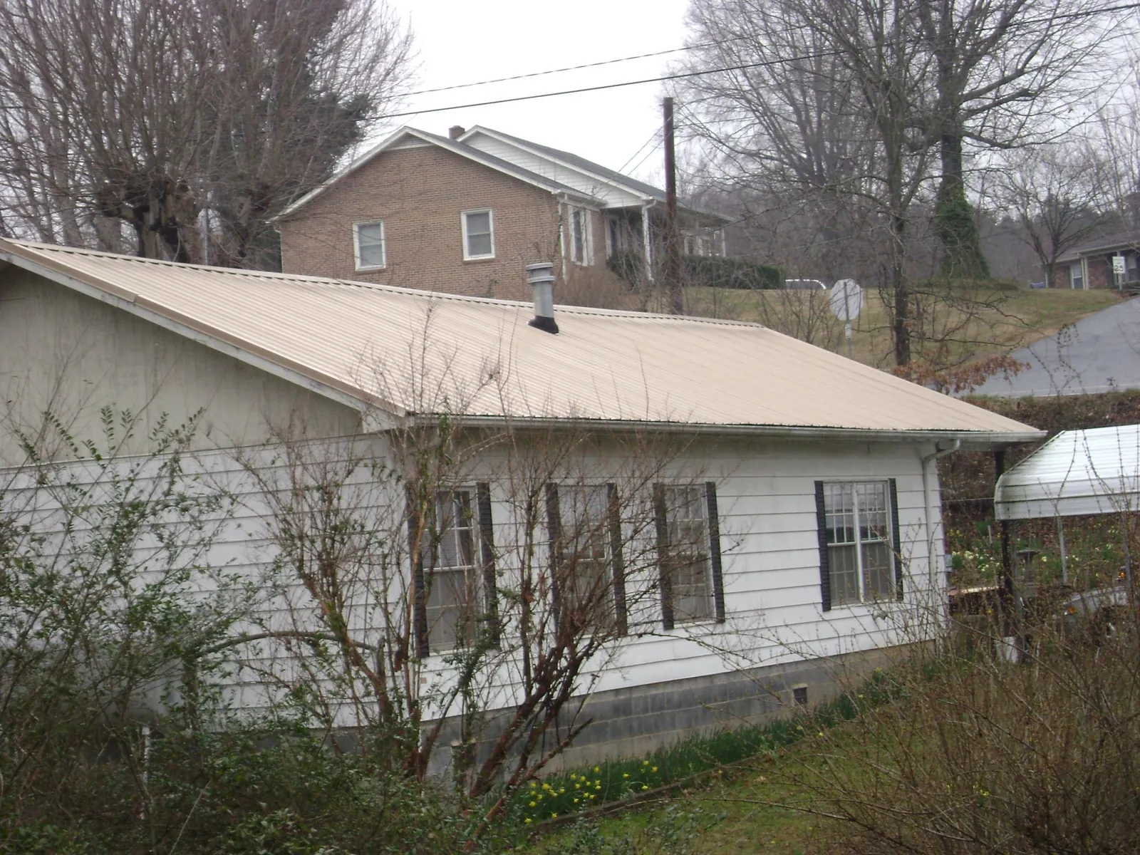 Tan metal roof on a white sided house set into a hillside — Commercial Roofing by Roofing Brothers in Georgetown